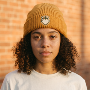 Woman wearing mustard Heart & Halo cuffed beanie against brick wall